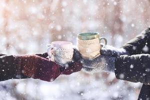 Couple hands in mittens take a mugs with hot tea in winter park photo