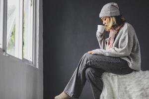 Lonely girl sitting and drinking a cup of coffee in front of the window on winter season photo